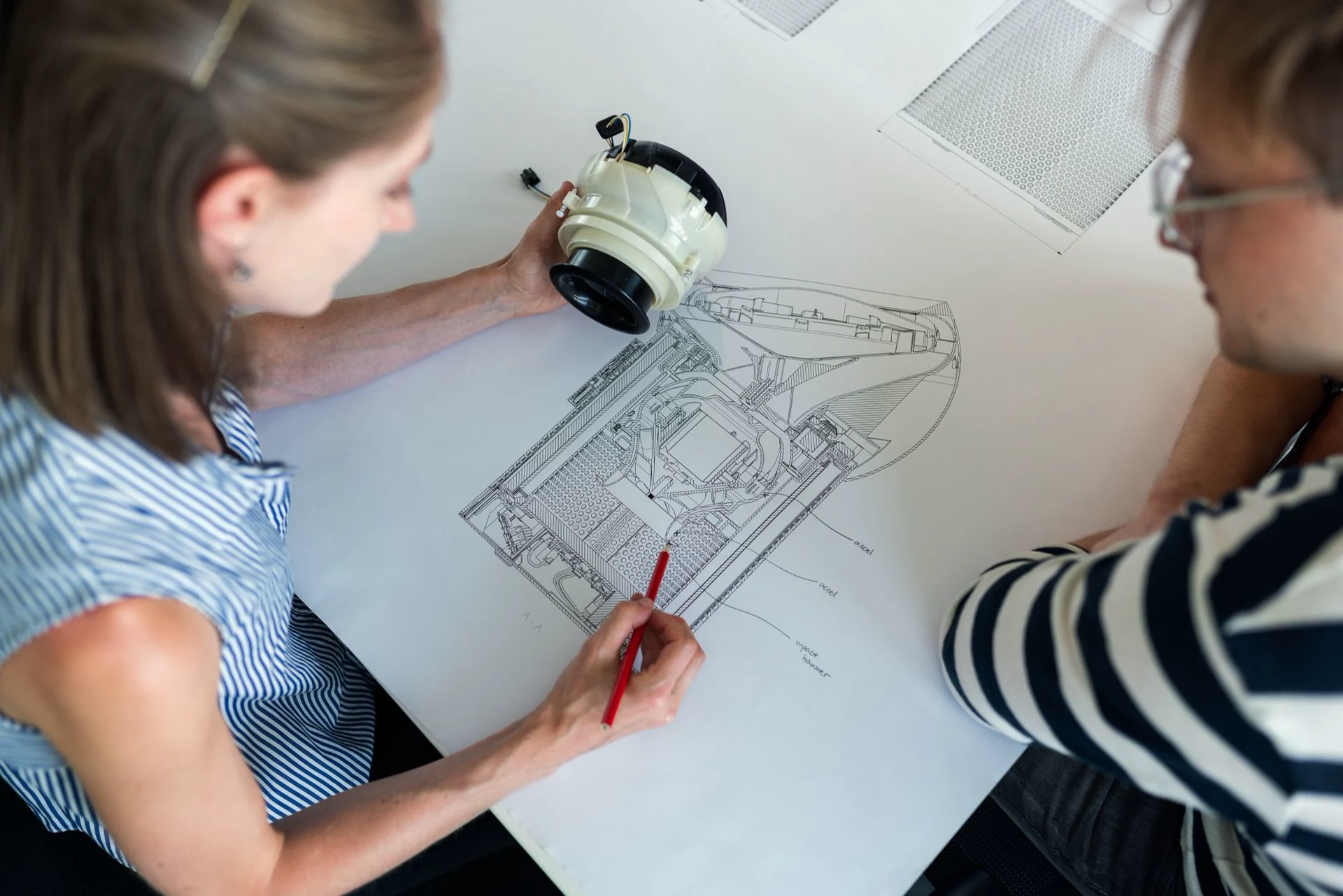 Engineers reviewing a technical drawing and a physical part; contextual stock photograph