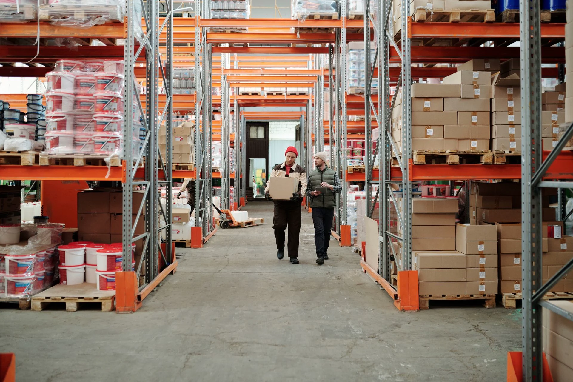 Two workers handling a package in a warehouse aisle; contextual stock photograph
